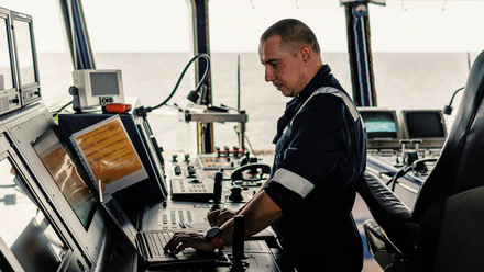 Seafarer in navy coveralls on the bridge on a laptop
